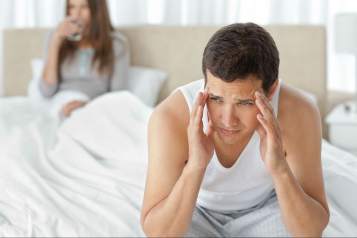Man having a headache sitting on the bed with his girlfriend